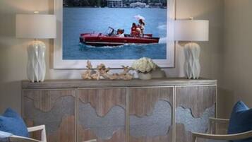 Uma sala de estar com um quadro grande de um barco vermelho na água, um armário de madeira com detalhes entalhados e duas poltronas azuis.