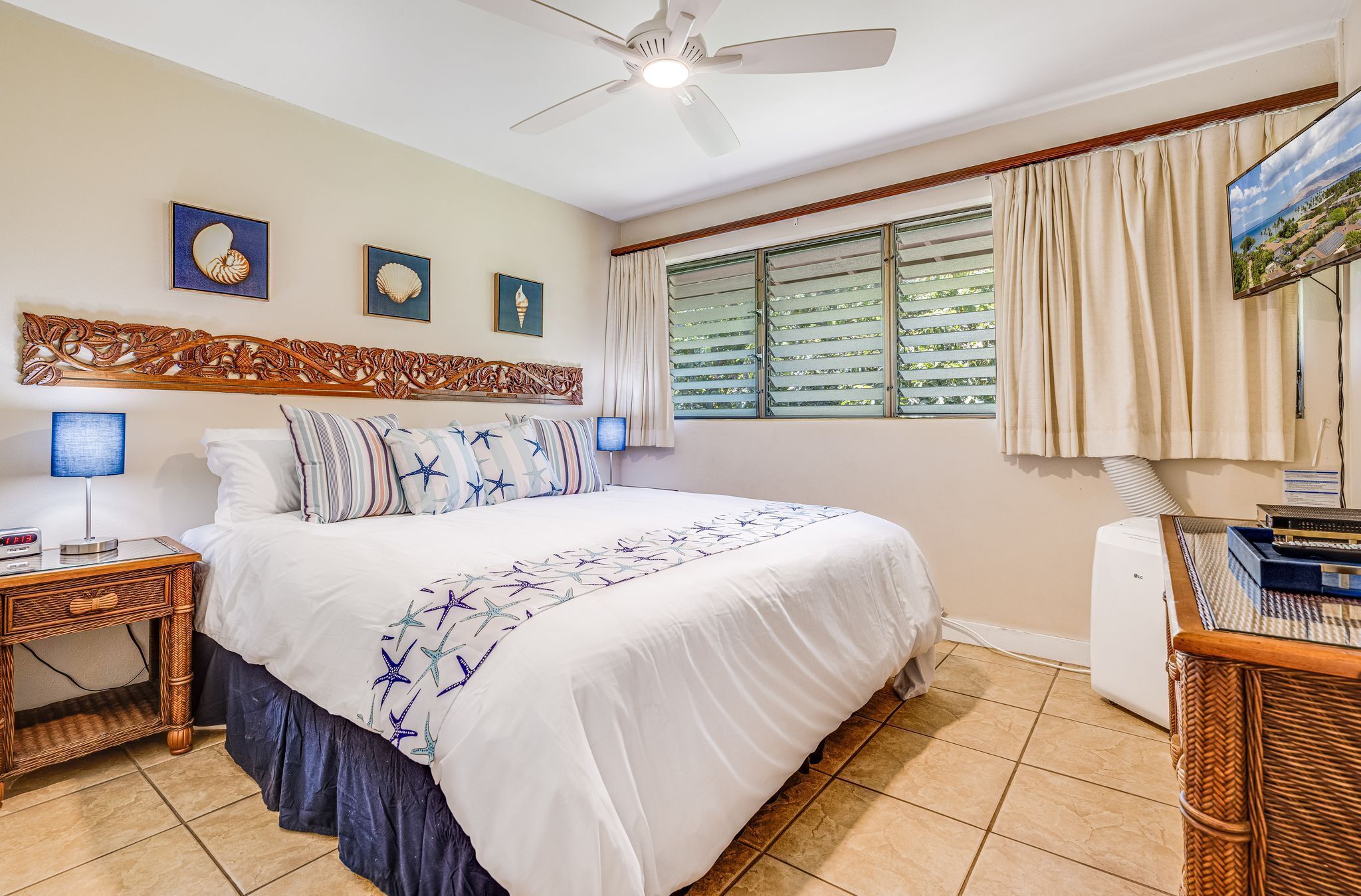 A bedroom with a large bed, a ceiling fan, a TV, and a window with blinds.