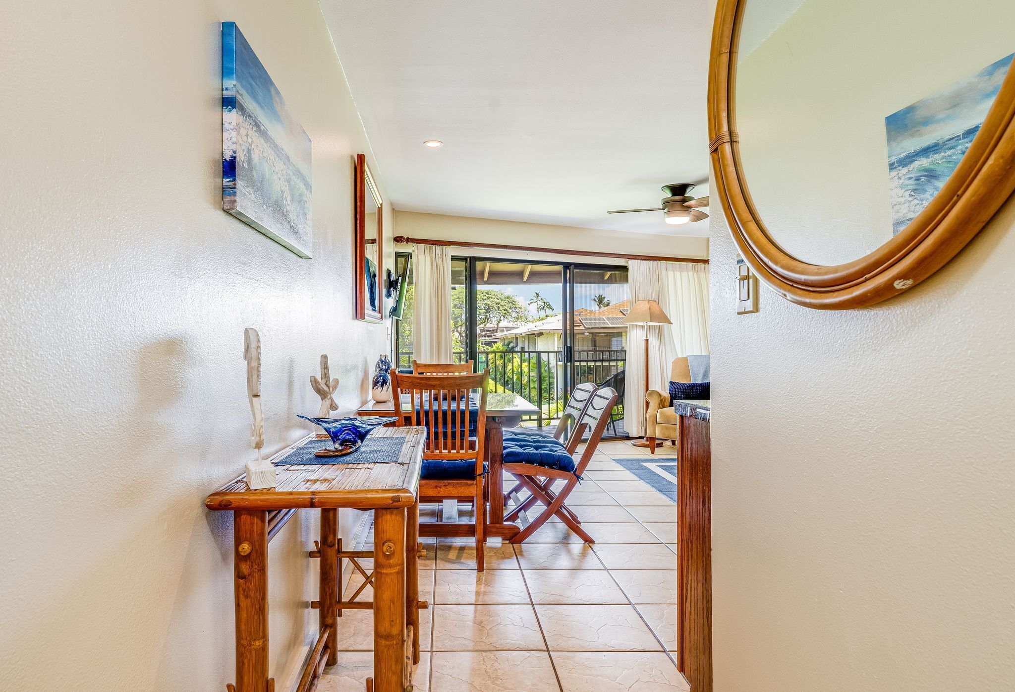 A dining area with a wooden table and chairs, a large mirror, and a view of the outdoors through a sliding glass door.
