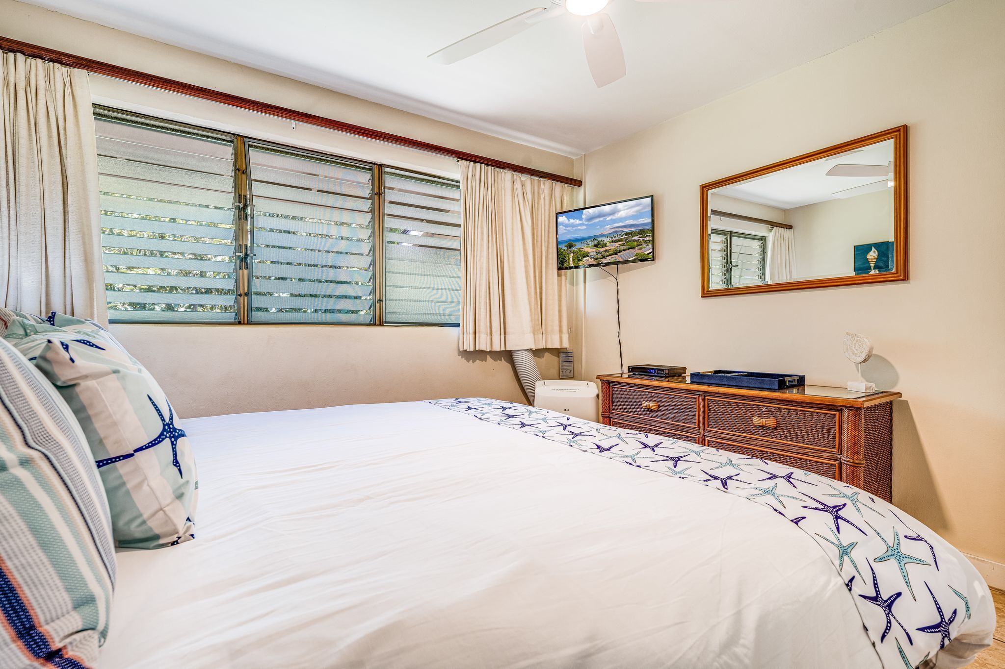 A hotel room with a large bed, a flat-screen TV, a wooden dresser, and a window with blinds.