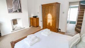 A bedroom with a bed, a wooden wardrobe, a small cabinet, a welcome sign, and a staircase. - The Townhouse (York)
