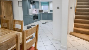 A modern kitchen with teal cabinets, a dining table with chairs, and a staircase leading to another level. - The Townhouse (York)