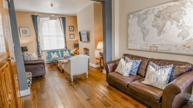 A living room with a brown leather sofa, a blue armchair, and a white armchair. There is a world map on the wall and a wooden floor. - The Townhouse (York)