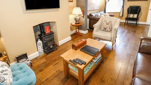 A living room with a fireplace, a television mounted on the wall, a sofa, a chair, and a coffee table with books and remote controls. - The Townhouse (York)