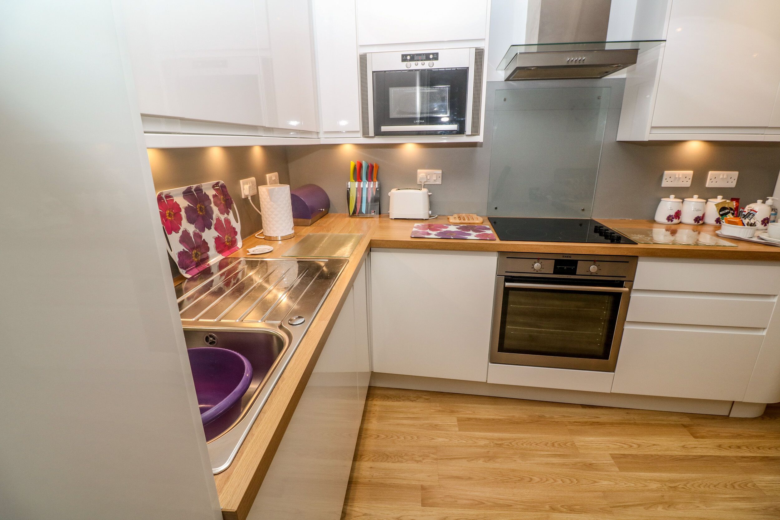A modern kitchen with white cabinets, a stainless steel oven, a built-in microwave, and a wooden countertop.
