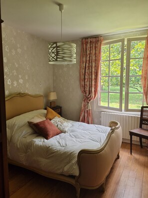 A bedroom with a bed, a chair, a window with curtains, a lamp, and a radiator.