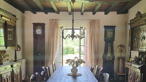 Un comedor con una larga mesa de madera, sillas, una araña y relojes en las paredes.