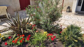 Un jardín con diversas plantas y flores, un sendero de piedra y una silla.