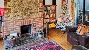 A cozy living room with a stone fireplace, a bookshelf, a Christmas tree, and a leather sofa. - A lovely traditional Norfolk barn conversion in the heart of the coastline. (Sidestrand, near Cromer)