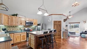 Una cocina amplia con armarios de madera, una isla grande con taburetes de bar, un reloj en la pared y una cabeza de venado montada.