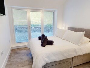 Un dormitorio con una cama grande, ropa de cama blanca y vistas al exterior a través de una puerta de cristal.