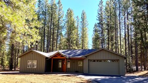 A single-story cabin with a garage, surrounded by tall pine trees. - Lovely Spring Home, Access to Pool (Black Butte Ranch)