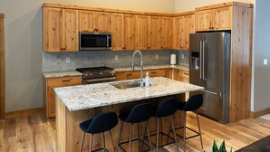 A modern kitchen with wooden cabinets, a stainless steel refrigerator, a built-in microwave, a gas stove, and a granite countertop. - Lovely Spring Home, Access to Pool (Black Butte Ranch)