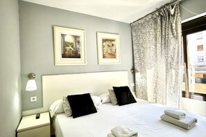 Une chambre d’hôtel avec un grand lit, deux tableaux encadrés au mur, une table de chevet avec une lampe et une fenêtre avec des rideaux.