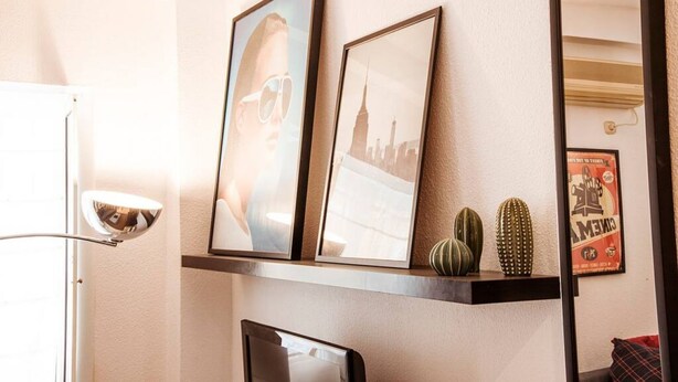 Een muur met ingelijste foto's, een spiegel en een plank met decoratieve objecten.