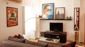Een woonkamer met een bank, salontafel, televisie en ingelijste foto's aan de muur.