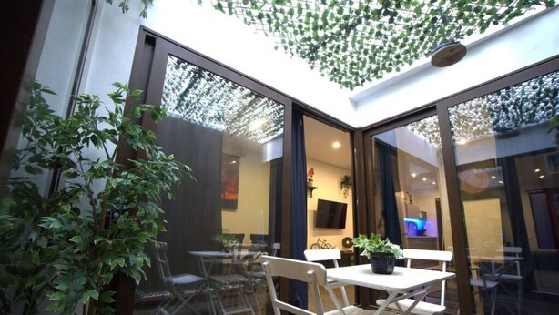 Un patio interior moderno con puertas de vidrio, una mesa de comedor, sillas y plantas en macetas.