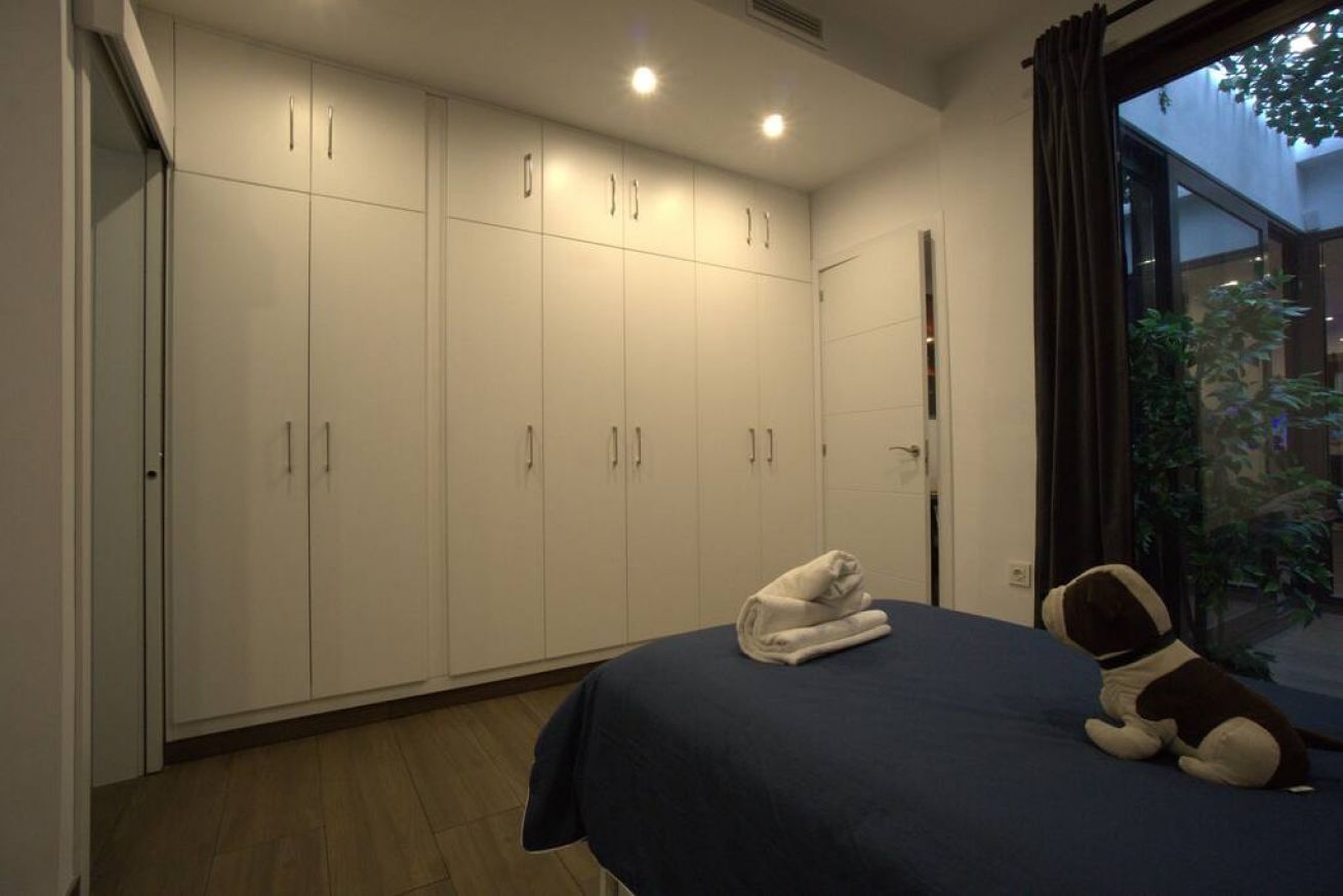 A bedroom with a large wardrobe, a bed with a dark blue bedspread, and a small stuffed animal on the bed.