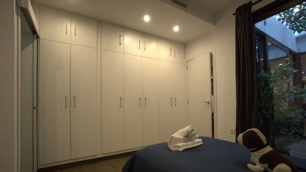 A bedroom with a large wardrobe, a bed with a dark blue bedspread, and a small stuffed animal on the bed.