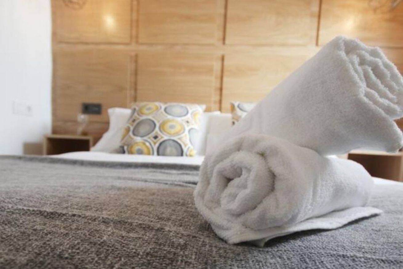 Un lit bien fait, avec une serviette blanche roulée, un oreiller à motifs et une tête de lit en bois, dans une chambre d’hôtel.