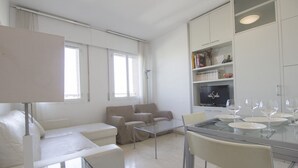 Uma sala de estar moderna com sofá, mesa de centro de vidro e um espaço de jantar com cadeiras e uma TV.