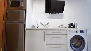 A compact kitchen with a built-in microwave, a stainless steel refrigerator, a washing machine, and a flat-screen TV. - Rental Sevilla Guadalquivir Dock (Sevilla)