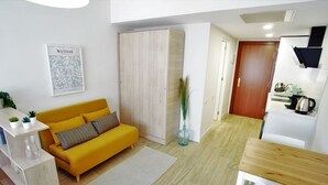 A modern living room with a yellow sofa, a wooden cabinet, and a kitchen area with a white refrigerator and a wooden table. - Rental Sevilla Guadalquivir Dock (Sevilla)