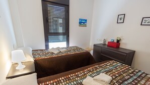 Ein Hotelzimmer mit zwei Betten, einem Schreibtisch mit Lampe, einem Schminktisch und einem Fenster mit Jalousien.