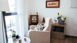 Ein gemütliches Wohnzimmer mit einem beigefarbenen Sofa, einem kleinen runden Tisch mit einer Tasse, einem Holznachttisch mit einer Pflanze und einem gerahmten Bild an der Wand.