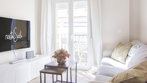 Een moderne woonkamer met een flatscreen televisie, een klein tafeltje met een vaas, een bank en een glazen schuifdeur naar een buitenruimte.