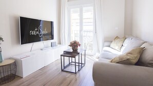 Een moderne woonkamer met een flatscreen televisie, een bank, een bijzettafeltje en uitzicht op buiten.
