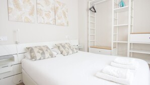 Een keurig opgemaakt slaapkamer met een bed, twee kussens, een nachtkastje en een garderobe met daarin hangende kleding.