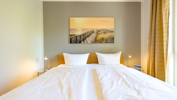 A double bed with white linens, a painting of a sunset over a beach, and a bedside table with a lamp. - House on the hill, Die Moderne 11 (Heringsdorf)