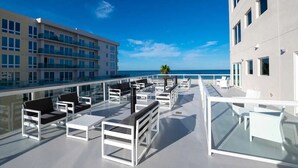 Una terraza en la azotea con mobiliario exterior, barandilla de cristal y vistas al mar.