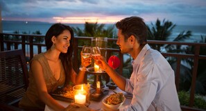 Et par spiser ved et bord med et stearinlys og et glas vin, mens de nyder udsigten over et smukt hav.