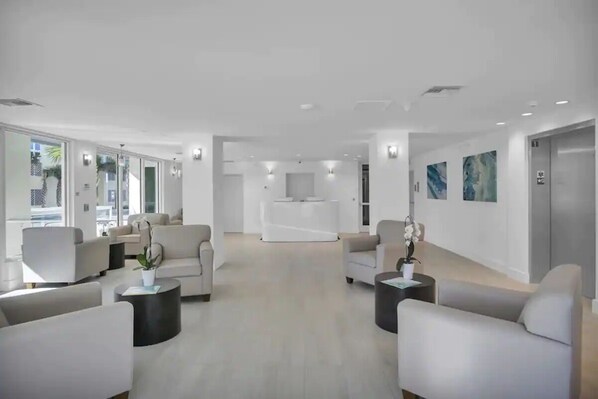 A modern, spacious lobby with a neutral color palette, featuring sofas, a reception desk, and artwork on the walls.