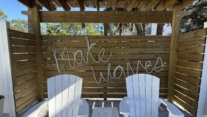 En pergola av trä med två vita Adirondack-stolar och ett litet bord, och på väggen står det "Skapa vågor".