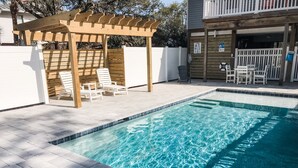 En swimmingpool med en pergola av trä och solstolar.