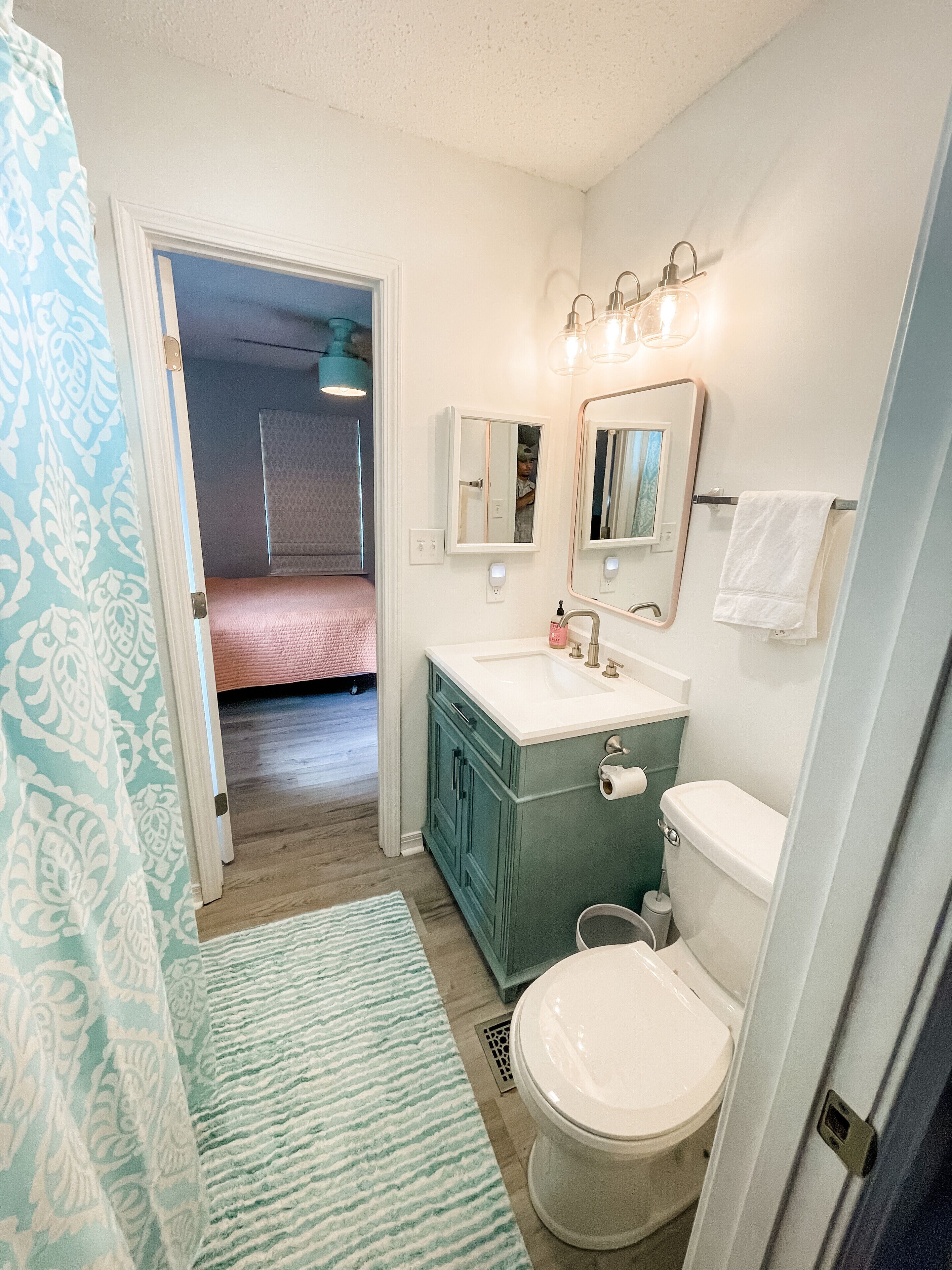 A bathroom with a sink, mirror, toilet, and a patterned shower curtain.