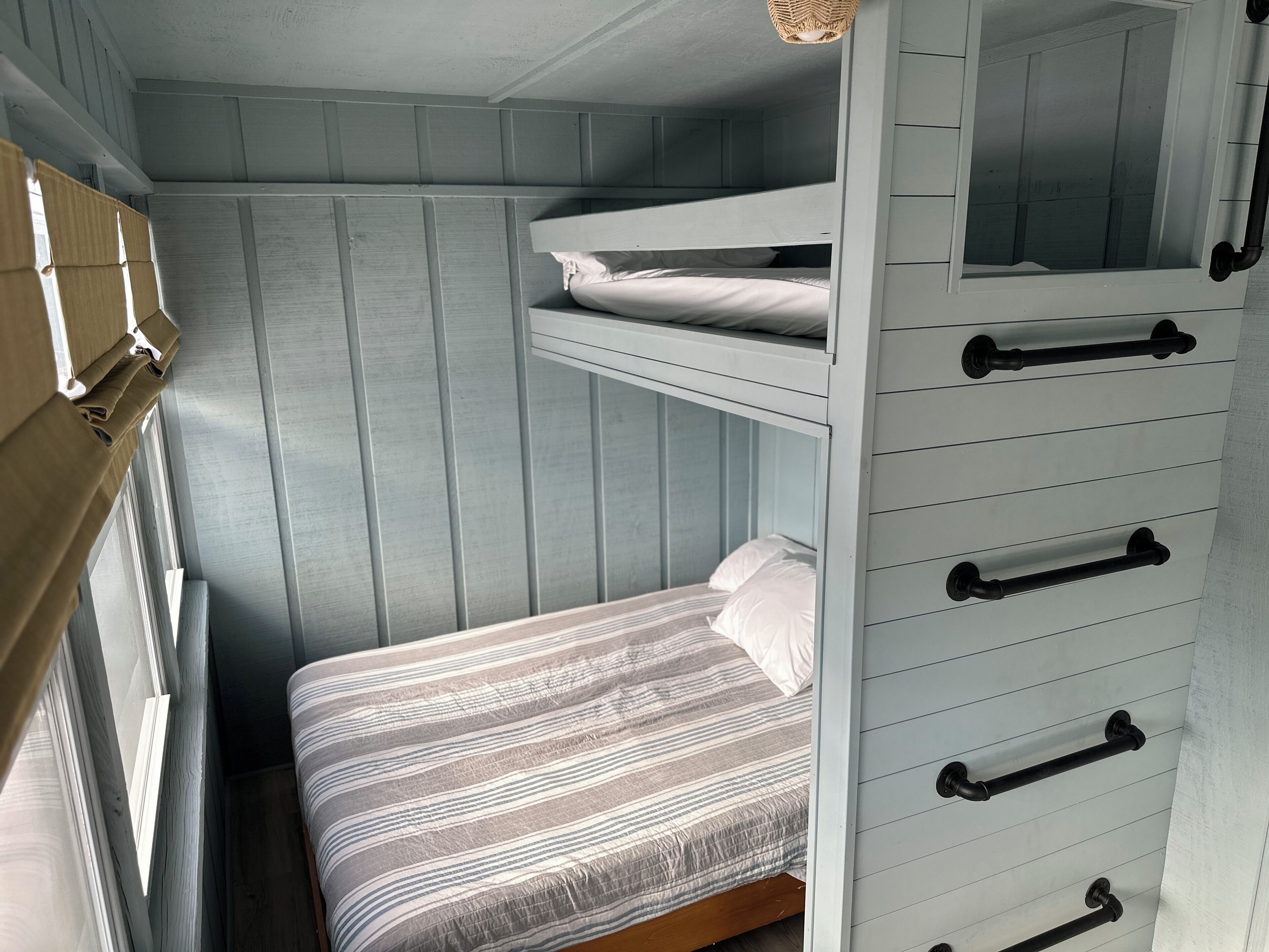 A bunk bed with a striped bedspread and a window with curtains.