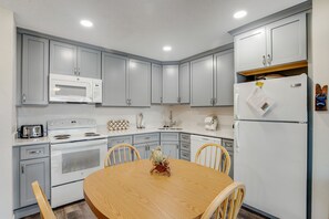 Compact kitchen area with a round table and four chairs, featuring a microwave, stove, toaster, and refrigerator.