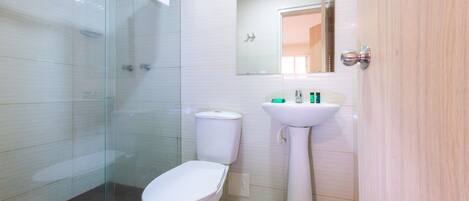 Un baño con cabina de ducha de vidrio, un inodoro blanco y un lavamanos pedestal.