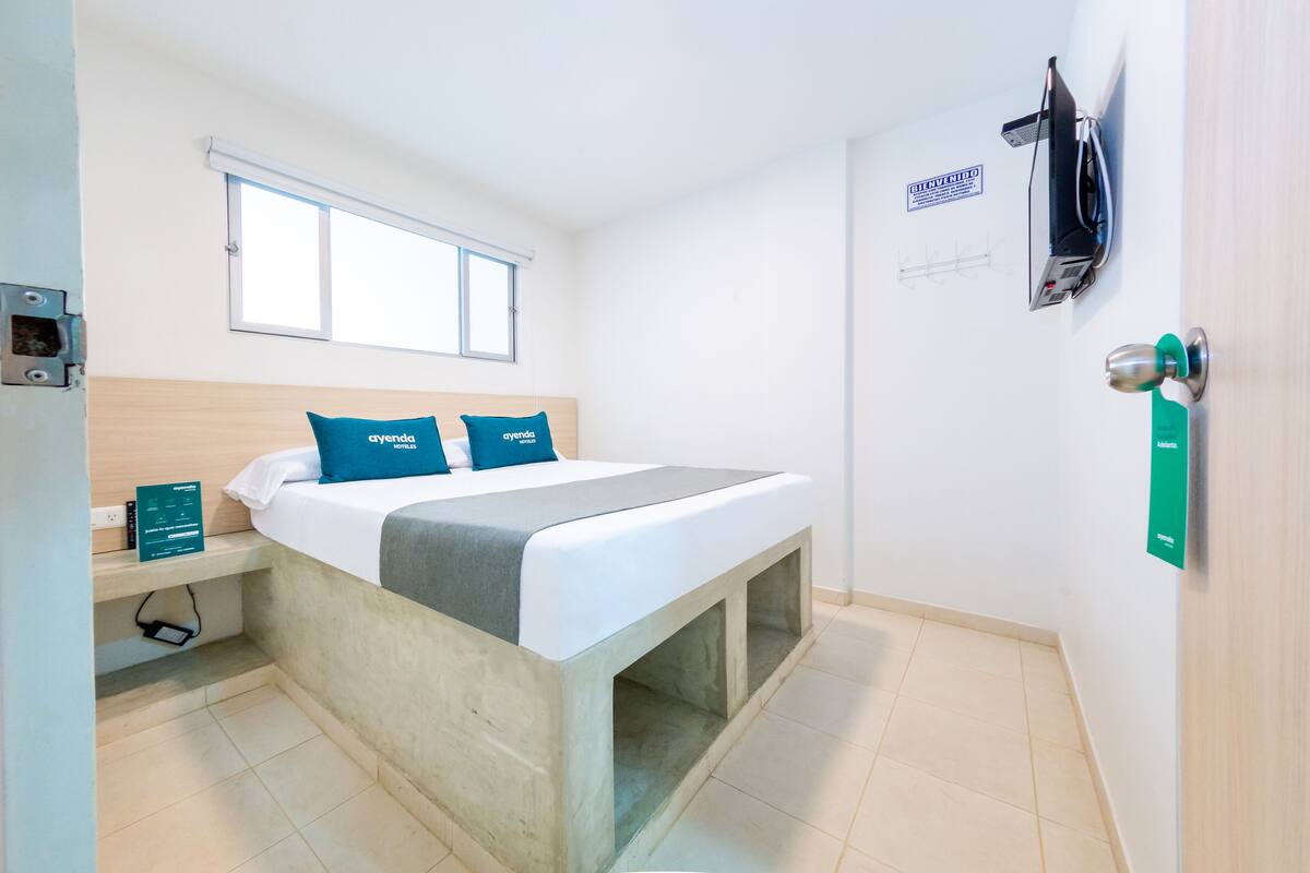 Une petite chambre moderne, équipée d’un lit, d’une fenêtre, d’un bureau et d’une porte sur laquelle est apposée une pancarte.