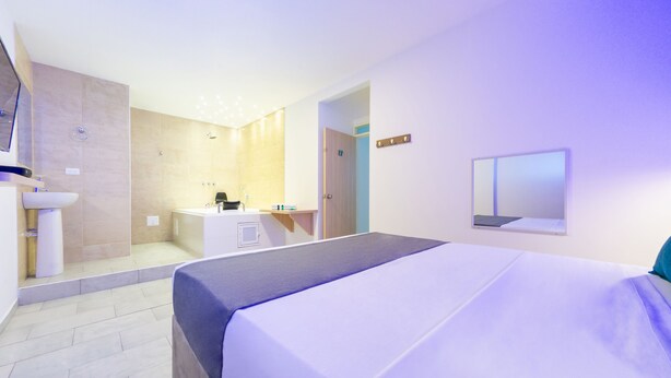 Une chambre d’hôtel moderne avec un grand lit, une salle de bain équipée d’un lavabo et d’une douche, et un petit bureau.
