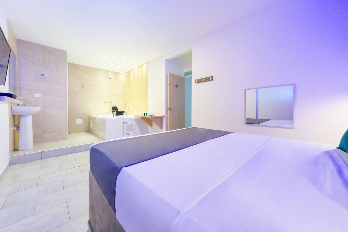Une chambre d’hôtel moderne avec un grand lit, une salle de bain équipée d’un lavabo et d’une douche, et un petit bureau.