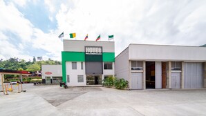 Un hôtel à la façade verte et blanche, orné de plusieurs drapeaux, et doté d’un parking où se trouve une moto.