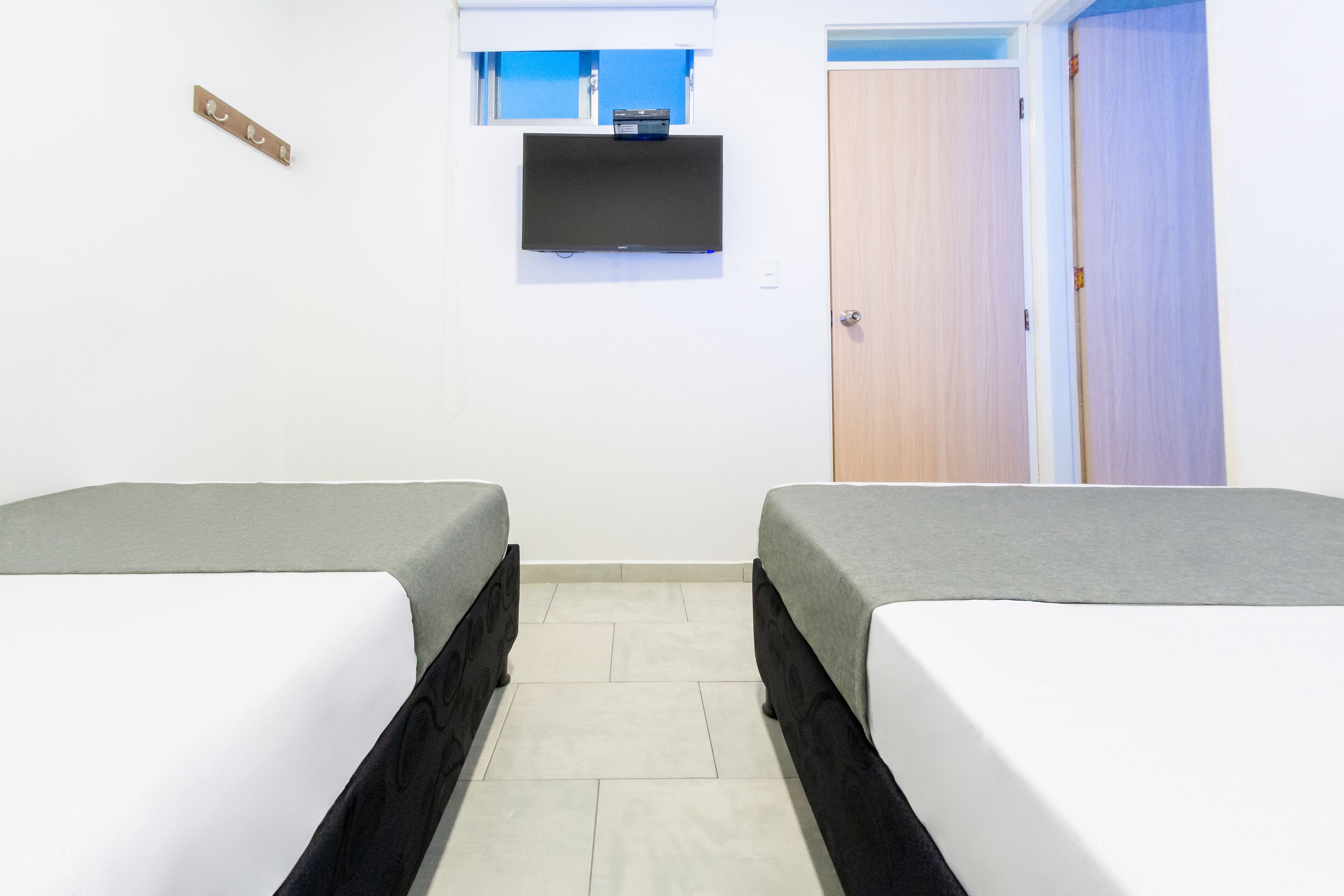 Une chambre avec deux lits, un téléviseur fixé au mur et une porte.