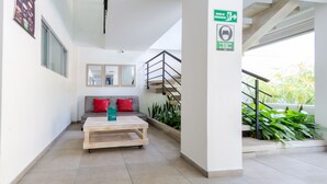 Un hall d’entrée moderne avec une table basse en bois, un canapé gris agrémenté de coussins rouges et un escalier doté d’une rampe en métal.
