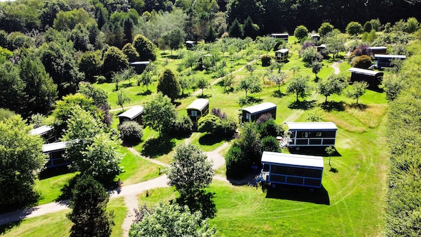 Ein Luftbild eines Campingplatzes mit mehreren Holzhütten, umgeben von üppiger Vegetation und Bäumen.
