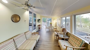 Ein gemütliches Interieur mit Deckenventilator, einem gemusterten Sofa und Blick durch große Fenster.